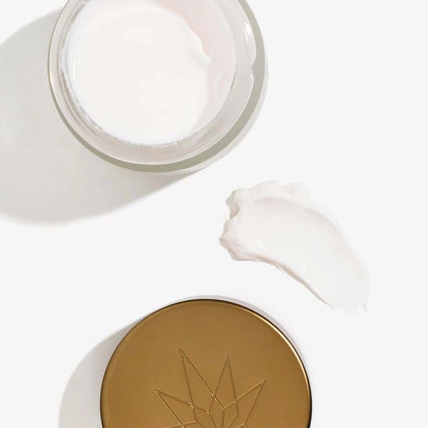 Een open verpakking en het deksel van de Nordic Cosmetics nachtcrème liggen naast een klodder van deze crème.