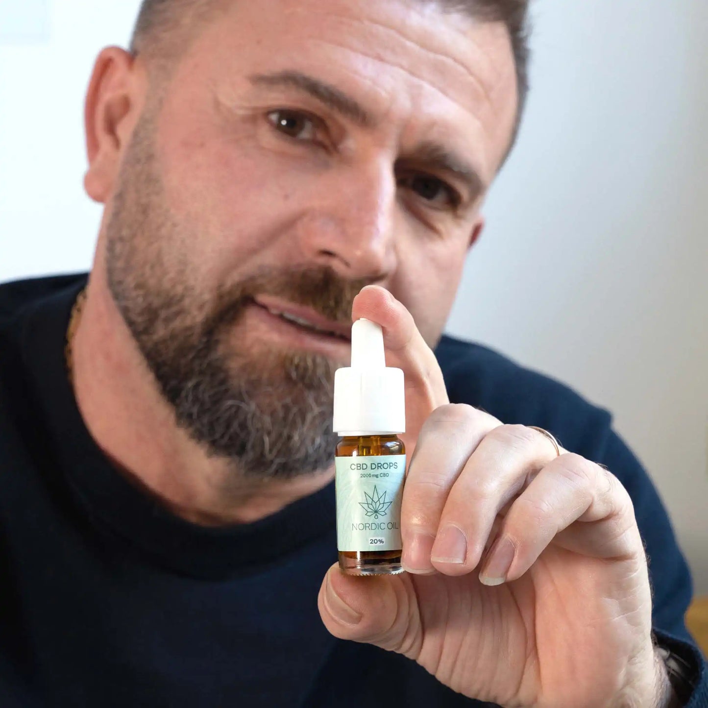 een man houdt de CBD olie in de camera terwijl hij glimlacht