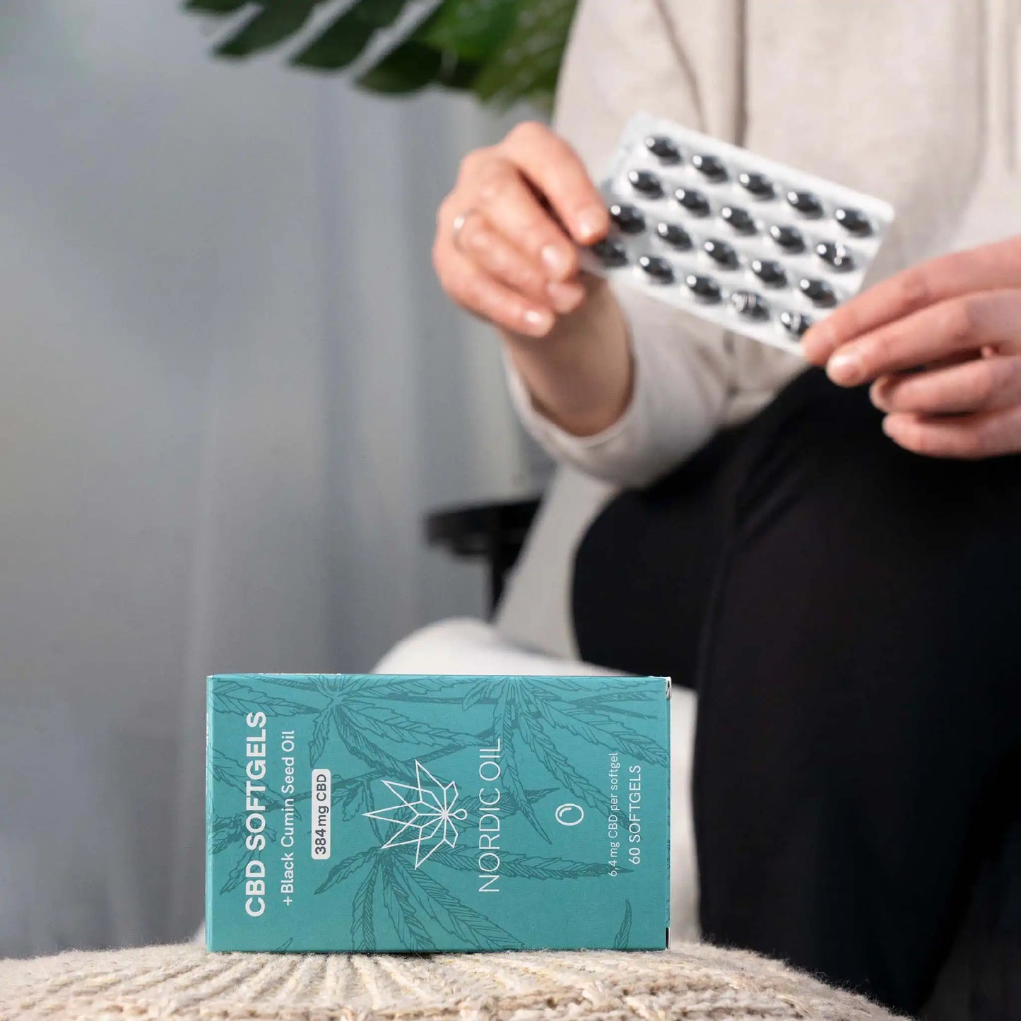 Op de voorgrond de verpakking van CBD-capsules; op de achtergrond houdt de klant de capsules vast.
